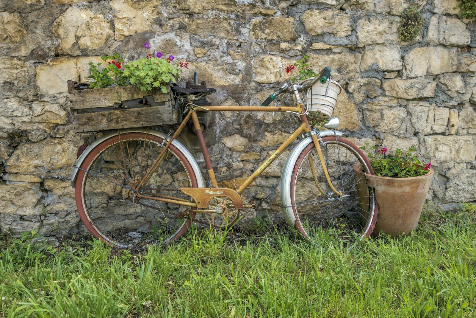 an old bicycle with a basket of flowers next to a stone wall